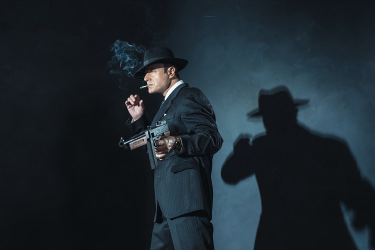 Retro 1940s film noir gangster with gun smoking cigarette.